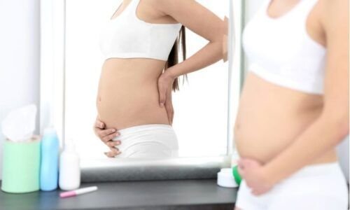 Mujer embarazada mirando su barriga en el espejo