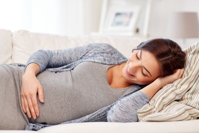 Mujer embarazada tumbada en el sofá tocándose la barriga