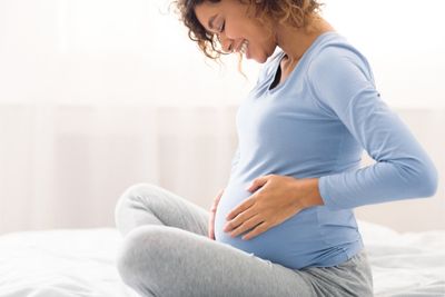 Mujer embarazada tocándose la barriga y sonriendo