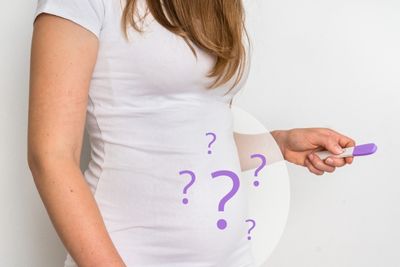 Mujer con signos de pregunta en la barriga y test de embarazo en la mano