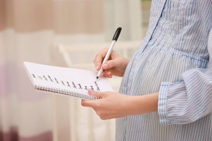 Mujer embarazada con camisa azul y libreta con nombres de bebé