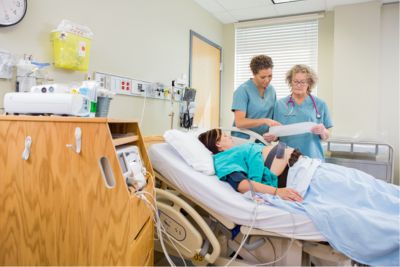 Mujer embarazada en habitación de hospital, mientras 2 enfermeras miran el plan de parto
