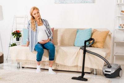 Mujer embarazada cansada sentada en el sofá con aspirador al lado